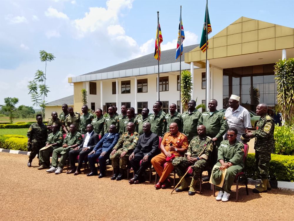 UBOS staff in military fatigues, with instructors and officials, in front of the National Leadership Institute building under three flags